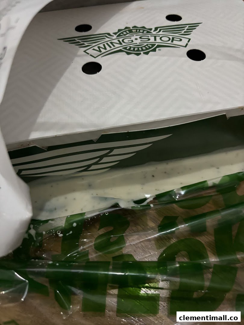 A Wingstop box with the logo visible, showing a creamy dip inside a plastic bag.