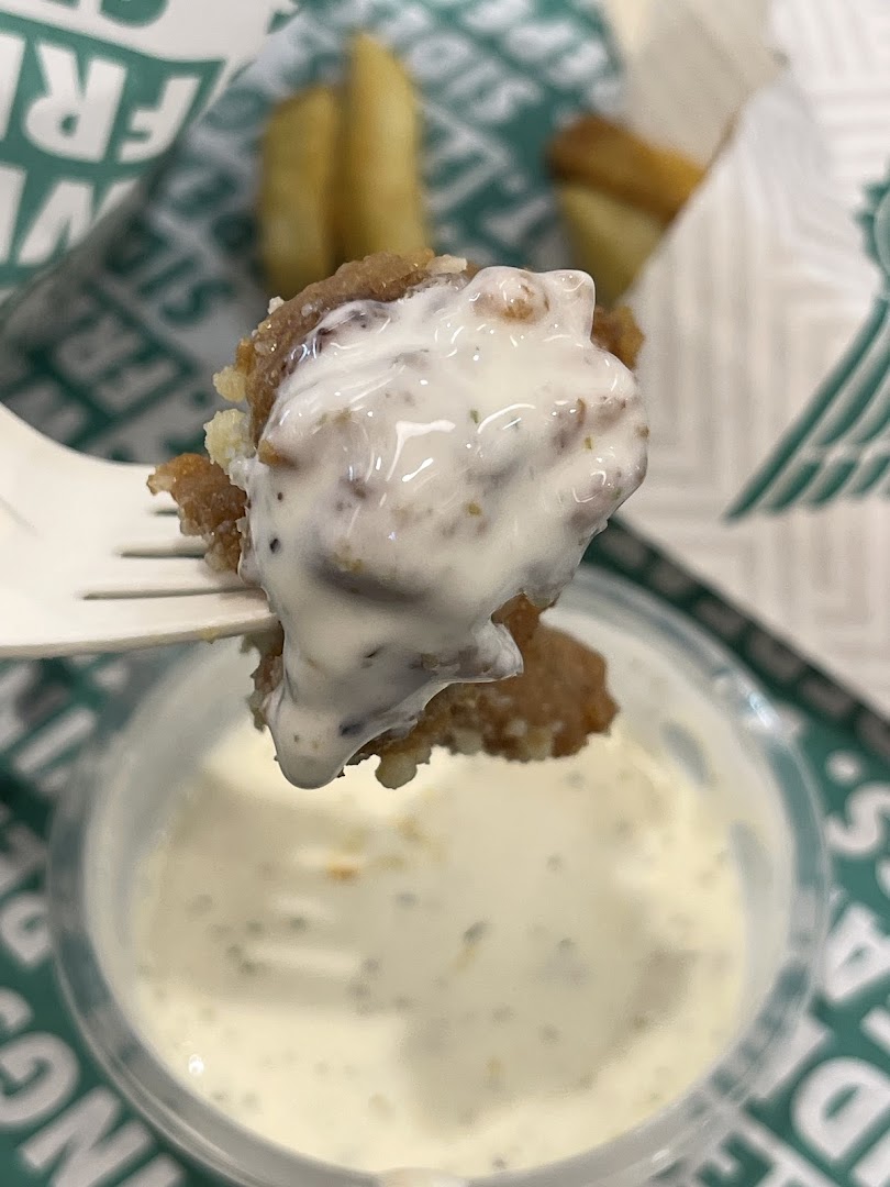 A close-up of a crispy chicken piece dipped in creamy ranch sauce from Wingstop.
