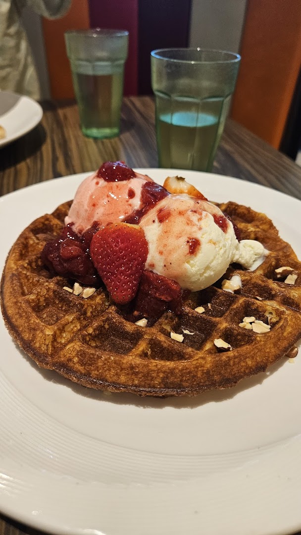 A golden waffle topped with strawberry and vanilla ice cream, fresh strawberries, and nuts.