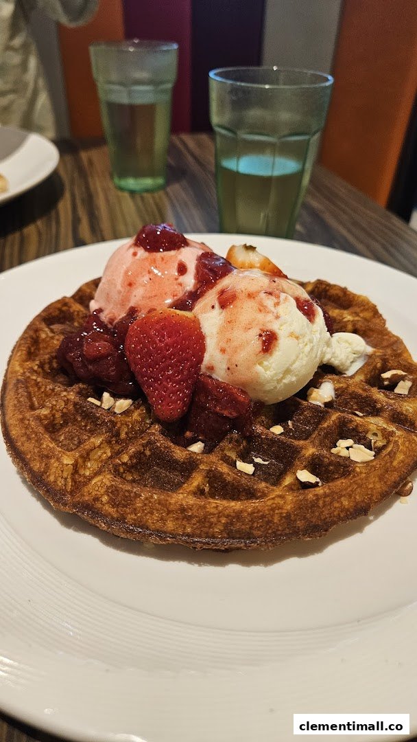 A golden waffle topped with strawberry and vanilla ice cream, fresh strawberries, and nuts.