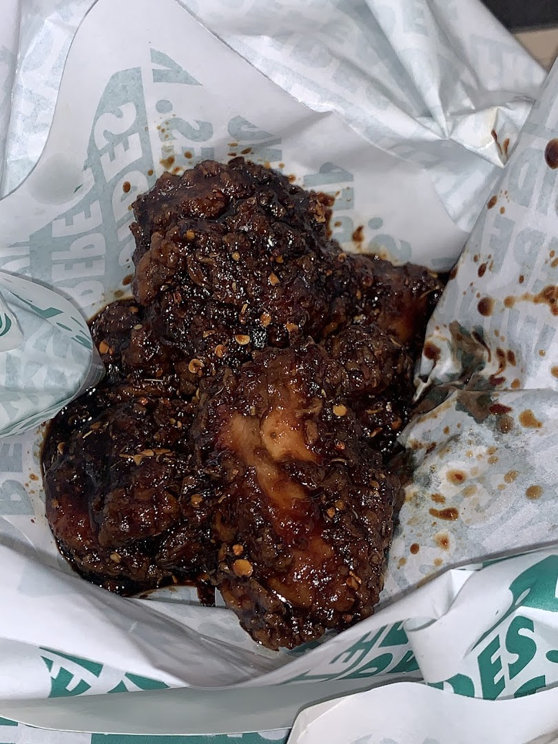 Close-up of saucy, seasoned chicken wings served in a Wingstop branded wrapper.