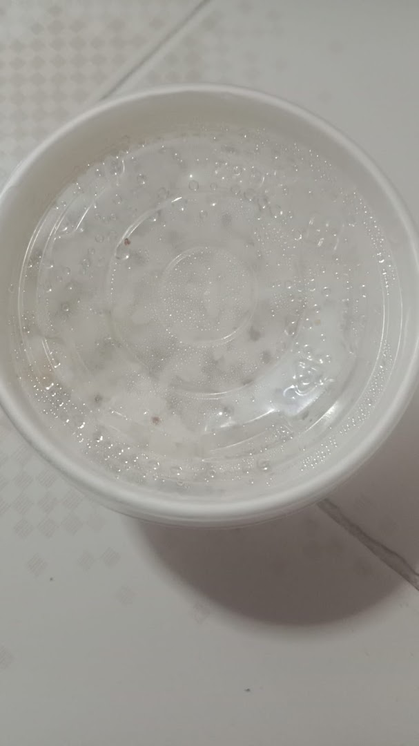 A white takeout container with a clear, condensation-covered lid, likely holding food.