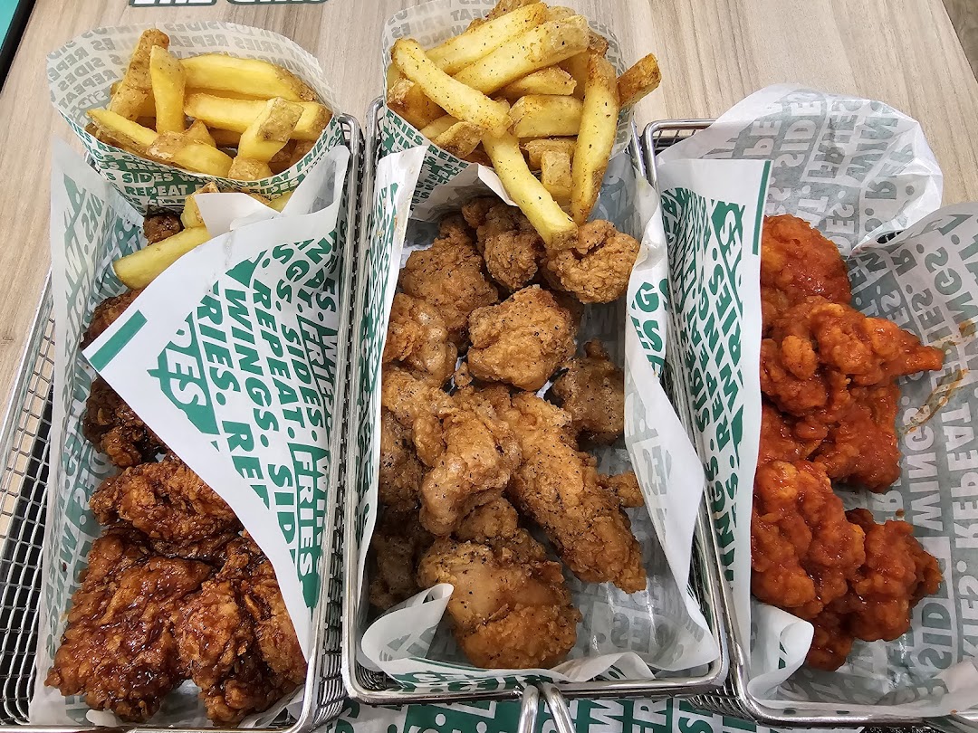 Three baskets of Wingstop chicken wings, tenders, and fries on a table.