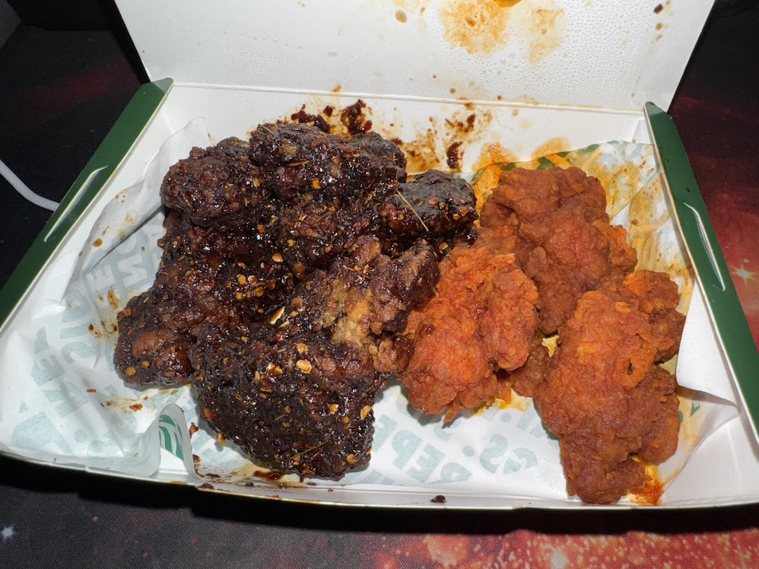 A box of Wingstop chicken featuring dark, saucy wings and crispy, red boneless chicken.