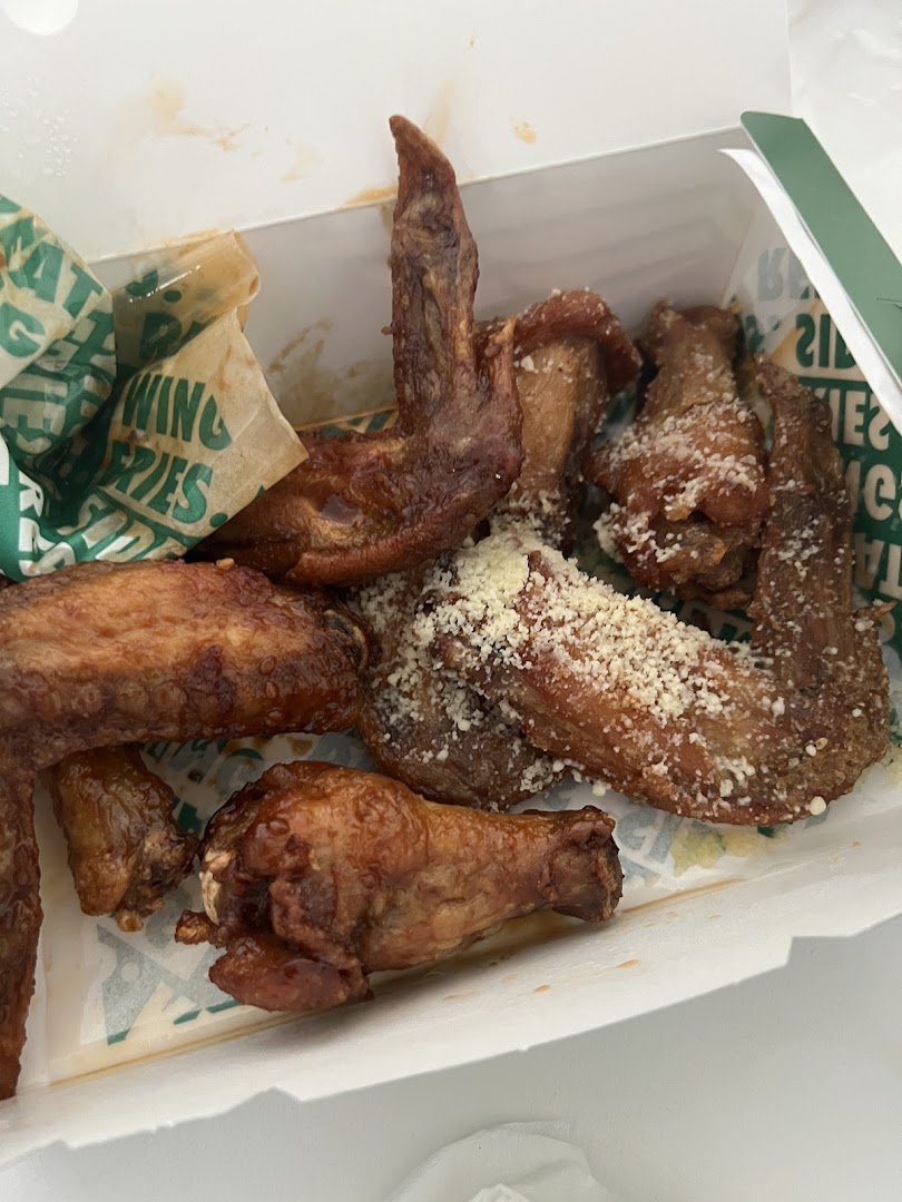 Close-up of delicious Wingstop chicken wings in a takeout box, some with parmesan.