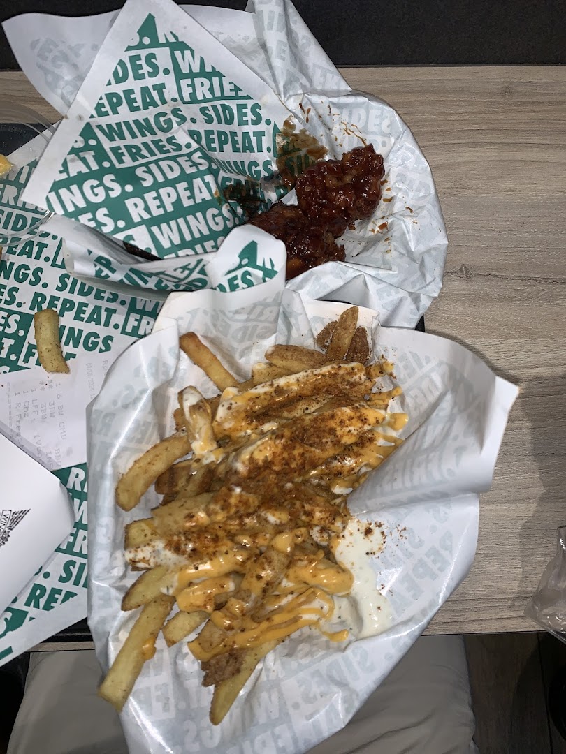 Two servings of Wingstop food, featuring saucy wings and loaded fries in branded paper.