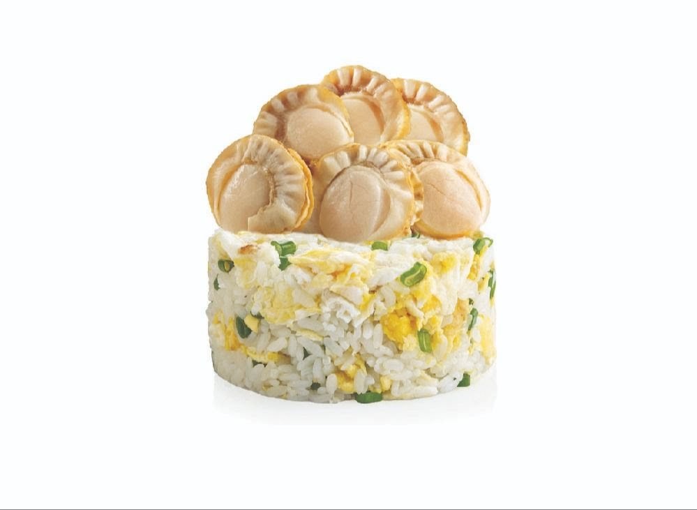 A cylindrical serving of fried rice topped with several plump scallops and garnished with spring onions.