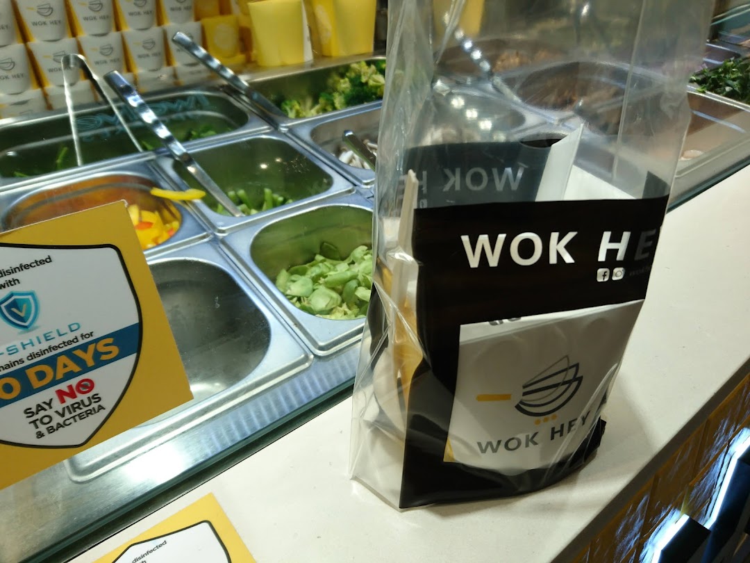 A WOK HEY food counter displaying fresh ingredients in steel bins and branded packaging, with a disinfection sign.