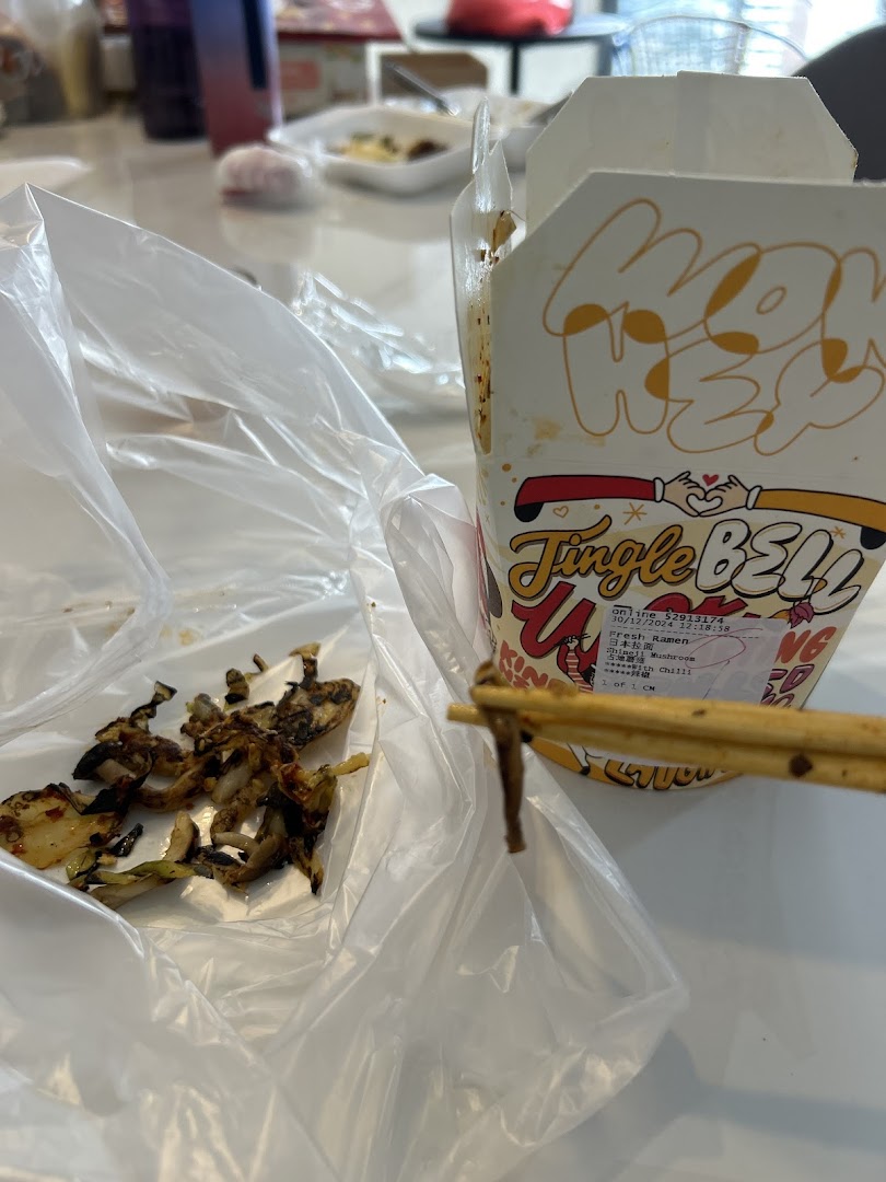 A Wok Hey food container with chopsticks holding a piece of food, on a table.