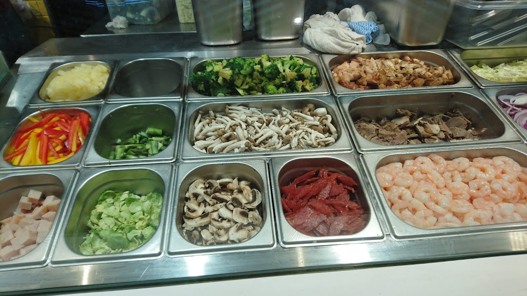A vibrant display of fresh ingredients like vegetables, meats, and seafood in metal trays, ready for custom wok dishes.