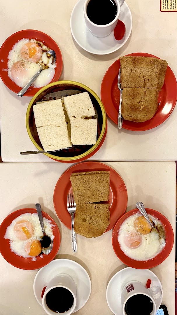 A table laden with traditional Singaporean breakfast: kaya toast, soft-boiled eggs, and coffee.