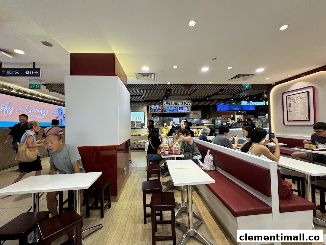 An interior view of Ya Kun Kaya Toast, showing customers seated at tables and benches in a bustling food court setting.