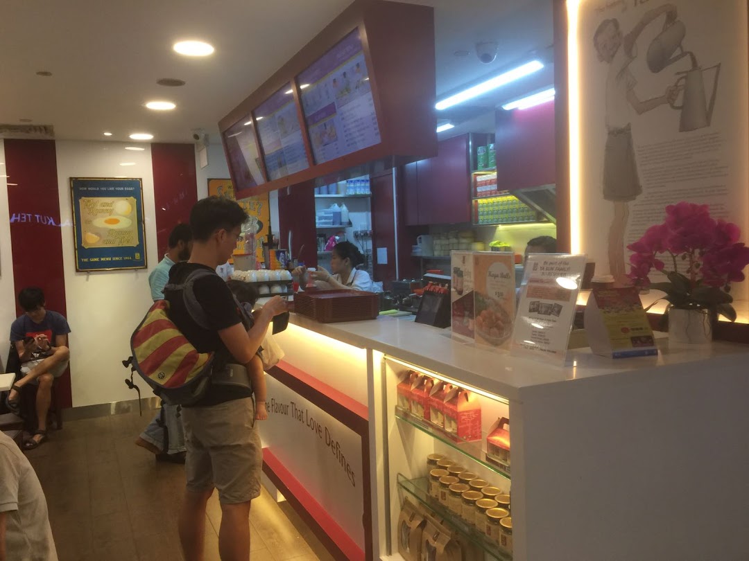 An interior view of Ya Kun Kaya Toast, showing the service counter, staff, customers, and product displays.