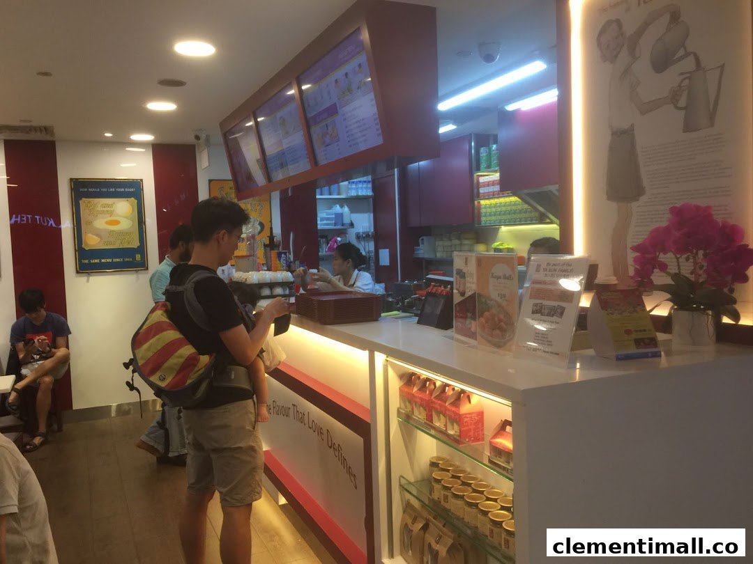 An interior view of Ya Kun Kaya Toast, showing the service counter, staff, customers, and product displays.