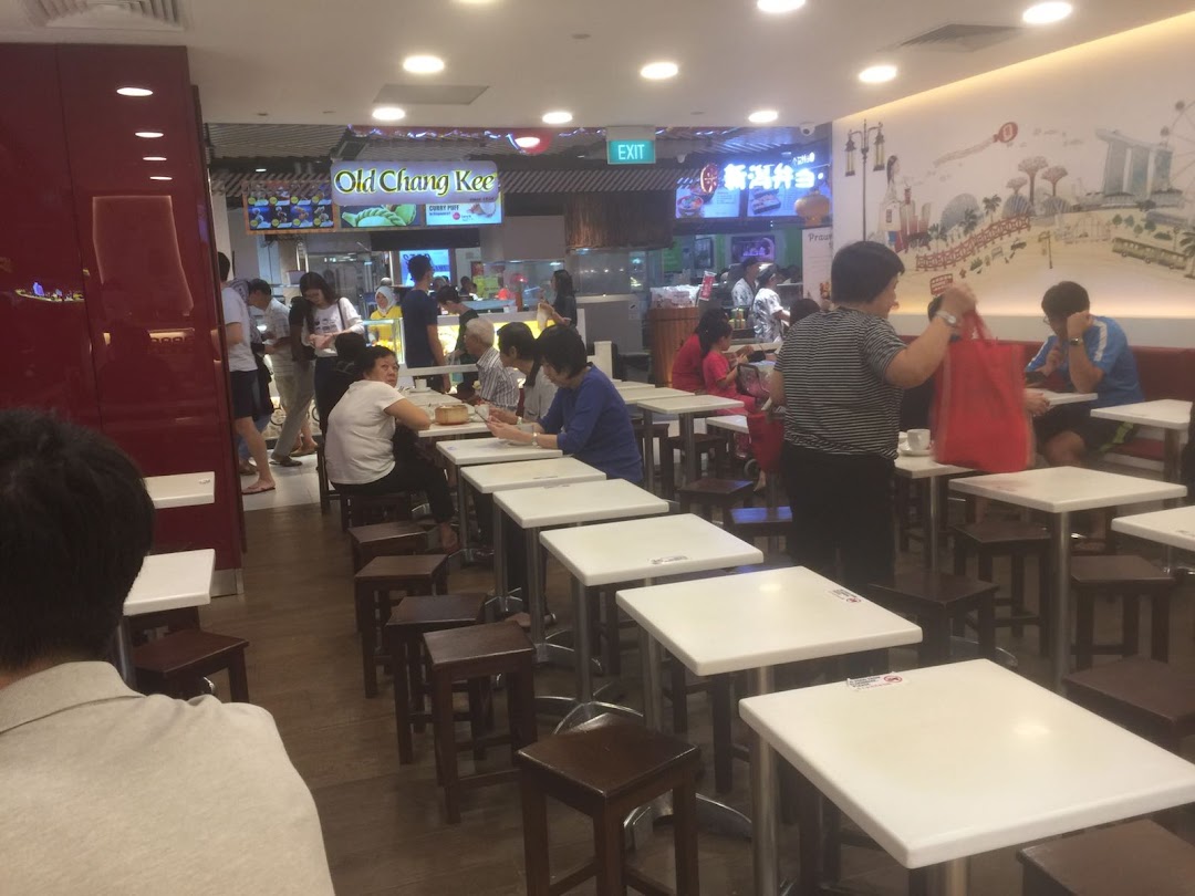 A bustling interior view of a food court with customers dining at white tables.
