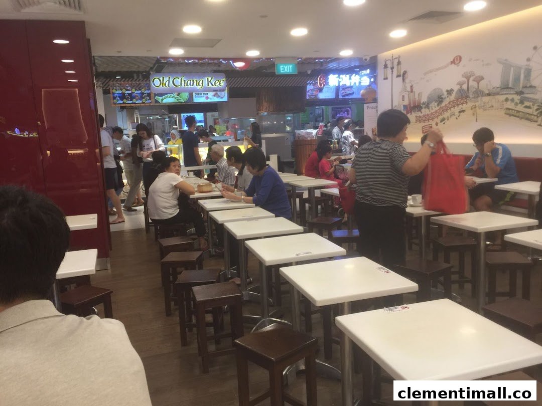 A bustling interior view of a food court with customers dining at white tables.