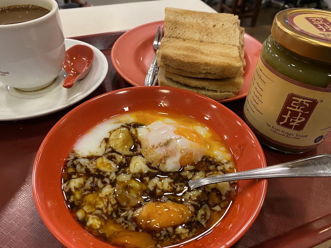 A classic Ya Kun Kaya Toast breakfast set featuring soft-boiled eggs, kaya toast, coffee, and a jar of kaya spread.