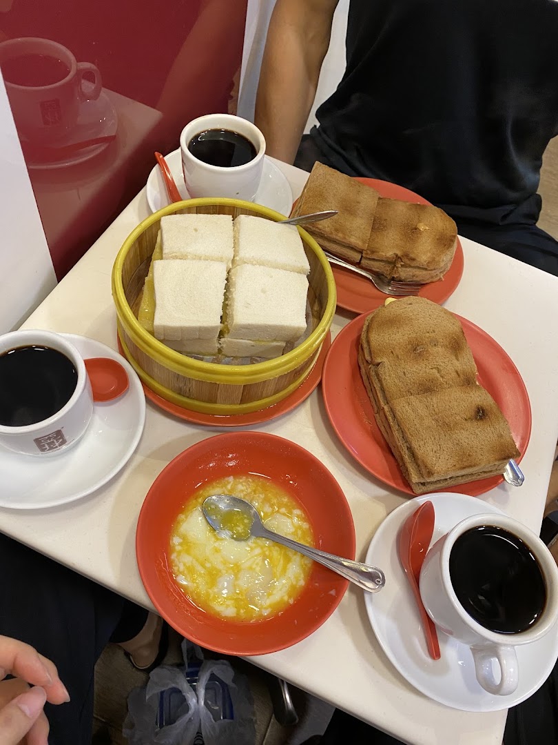 A table laden with traditional Singaporean breakfast items: kaya toast, soft-boiled eggs, and coffee.