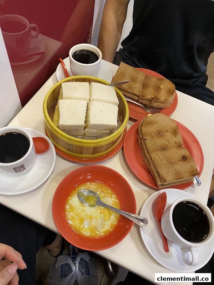 A table laden with traditional Singaporean breakfast items: kaya toast, soft-boiled eggs, and coffee.