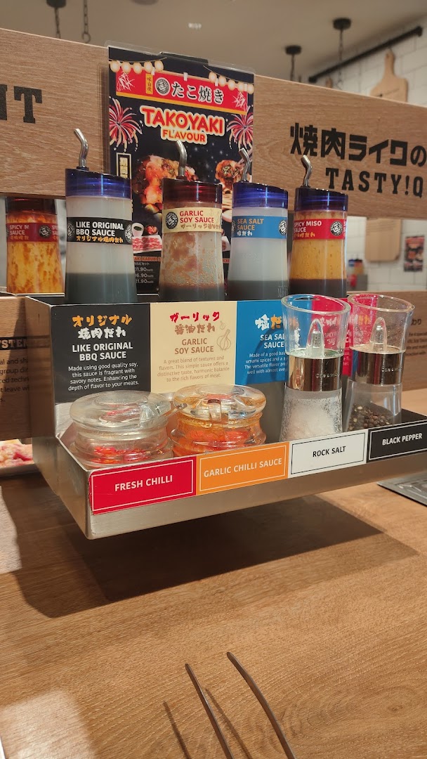 A close-up of Yakiniku Like's condiment station featuring various sauces, spices, and a Takoyaki promotion.