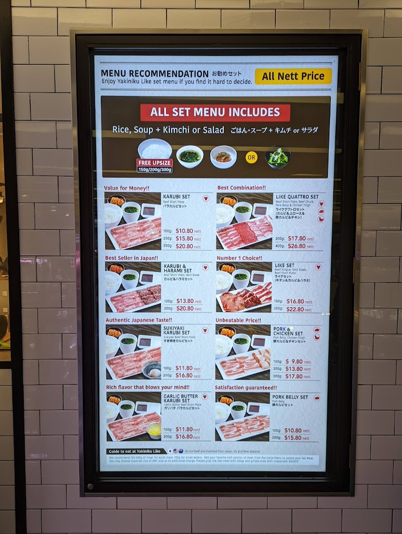 A brightly lit digital menu board displaying various yakiniku set meal options with prices and descriptions.