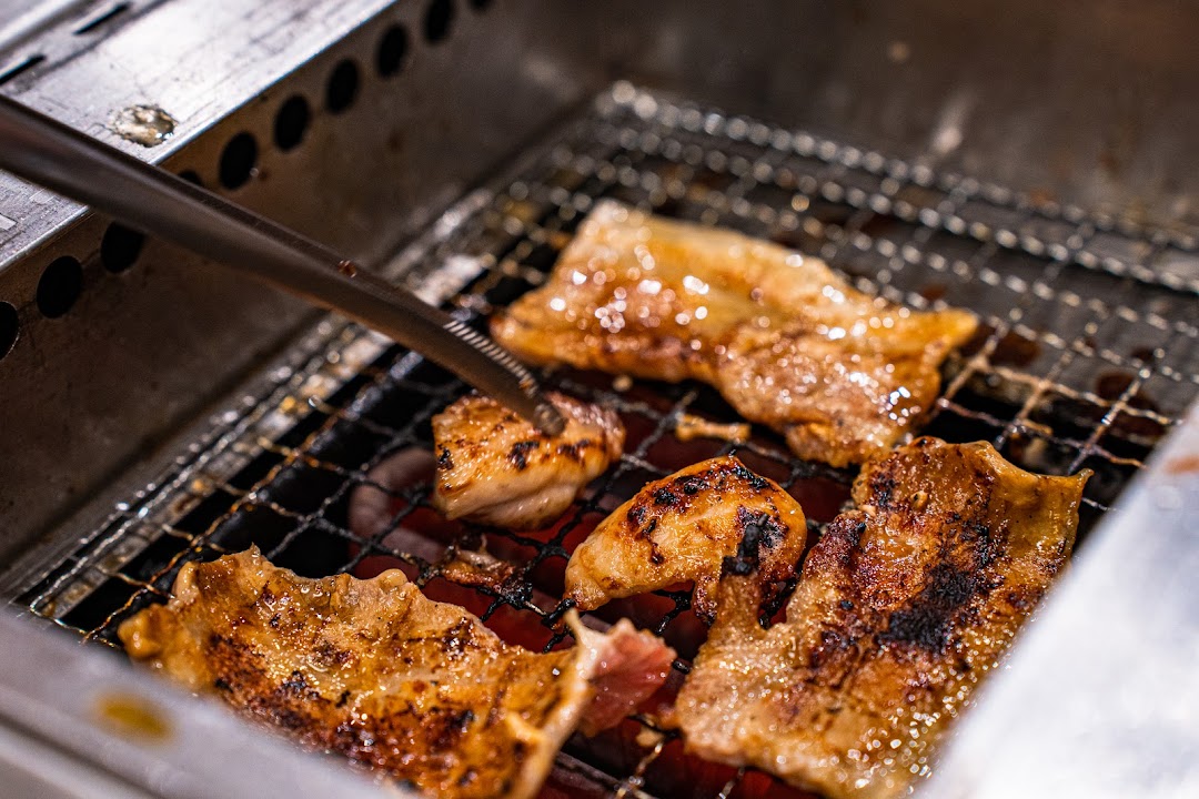Close-up of various meats sizzling on a yakiniku grill with tongs.