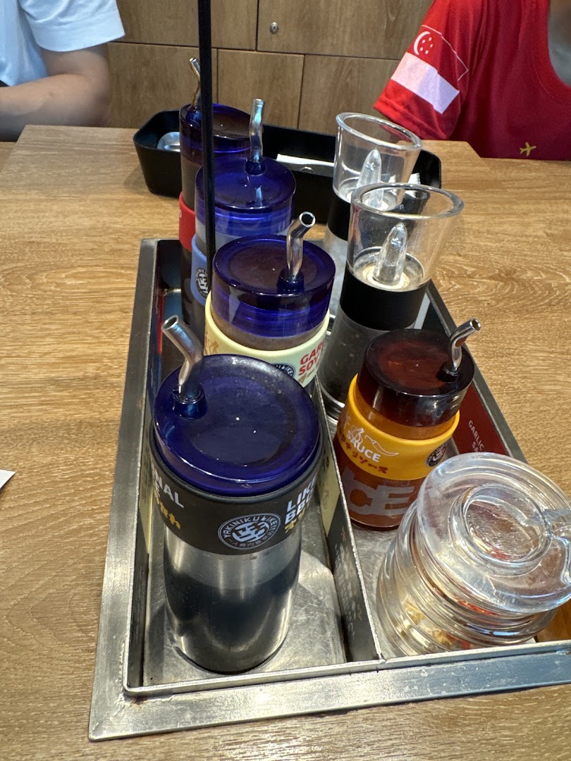 A close-up of a condiment caddy with various sauces, including garlic soy and BBQ, on a wooden table.