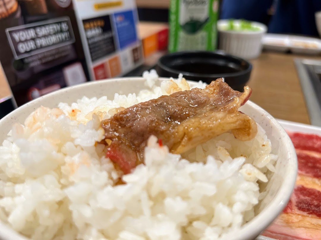 A close-up of a bowl of fluffy white rice topped with a piece of savory grilled yakiniku meat.