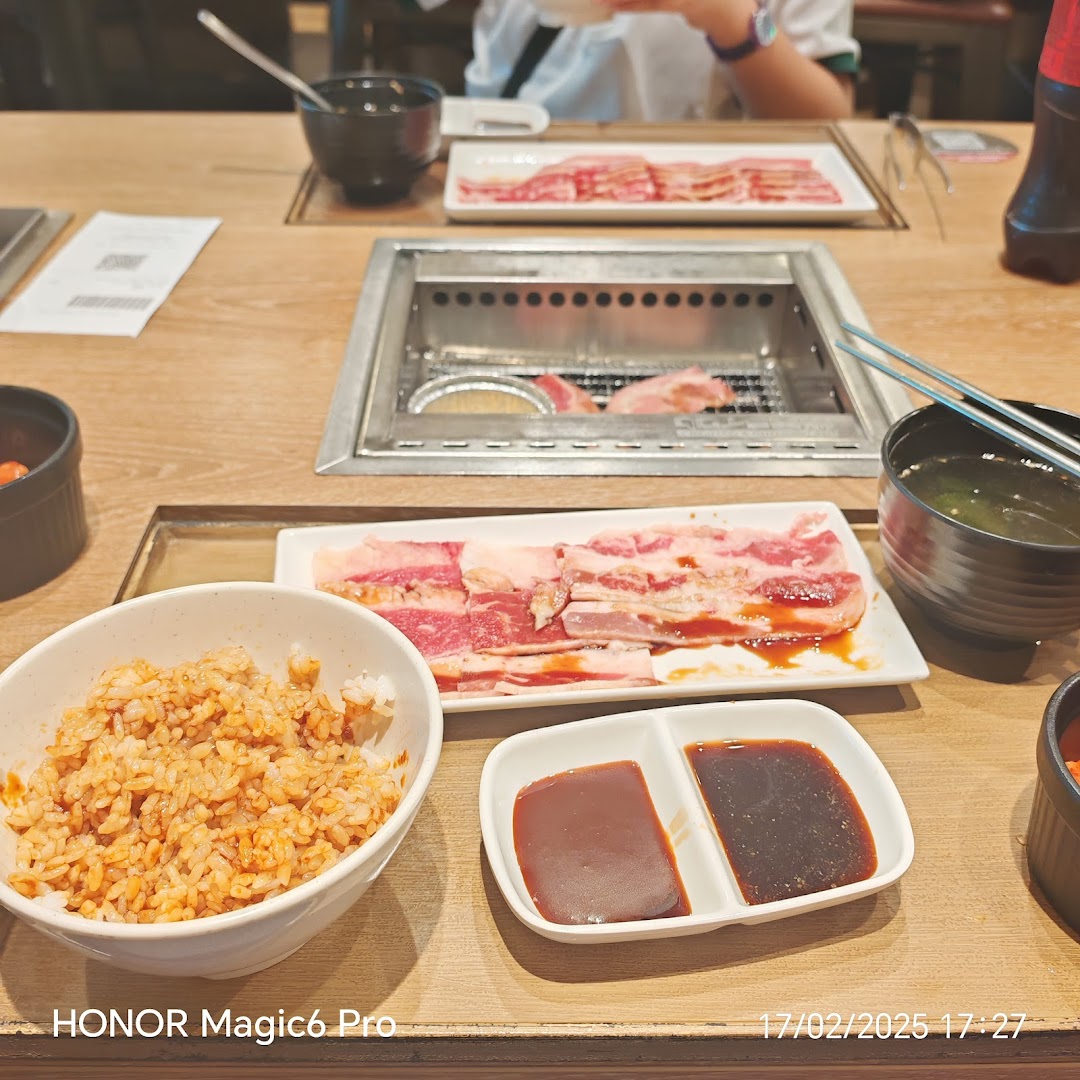 A close-up of a yakiniku meal featuring raw meat, rice, sauces, and a built-in grill at a table.