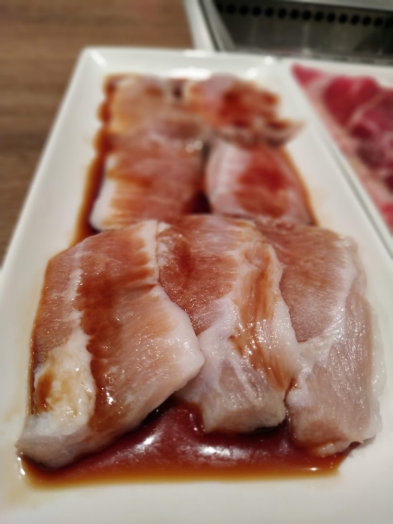 Close-up of marinated raw pork belly slices on a white plate, ready for grilling.