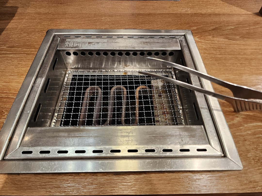 A close-up of an in-table yakiniku grill with metal tongs on a wooden table.