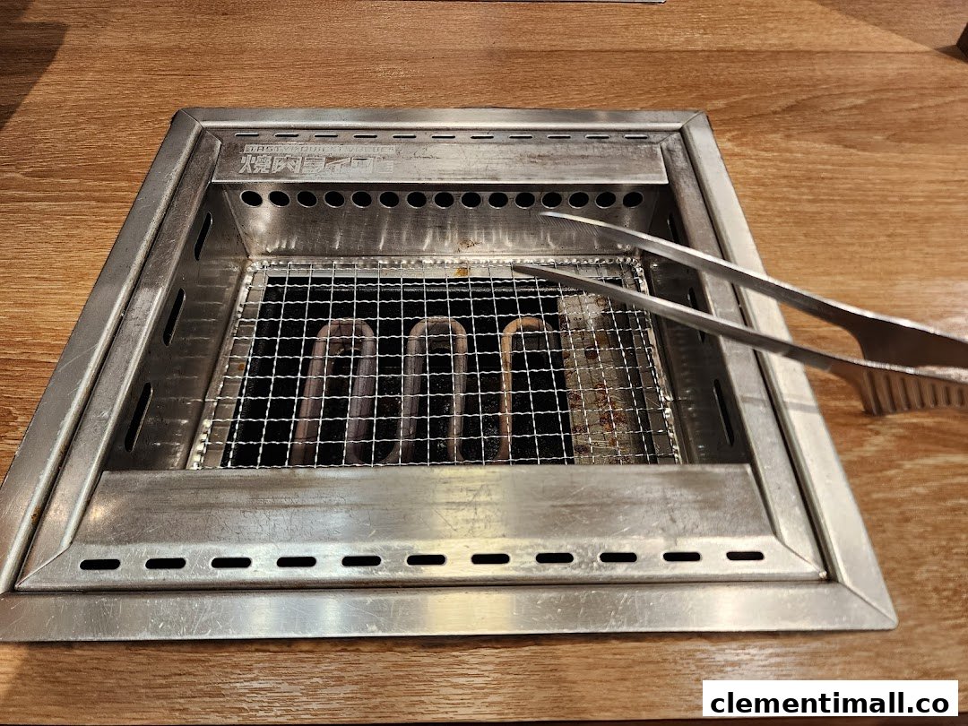 A close-up of an in-table yakiniku grill with metal tongs on a wooden table.