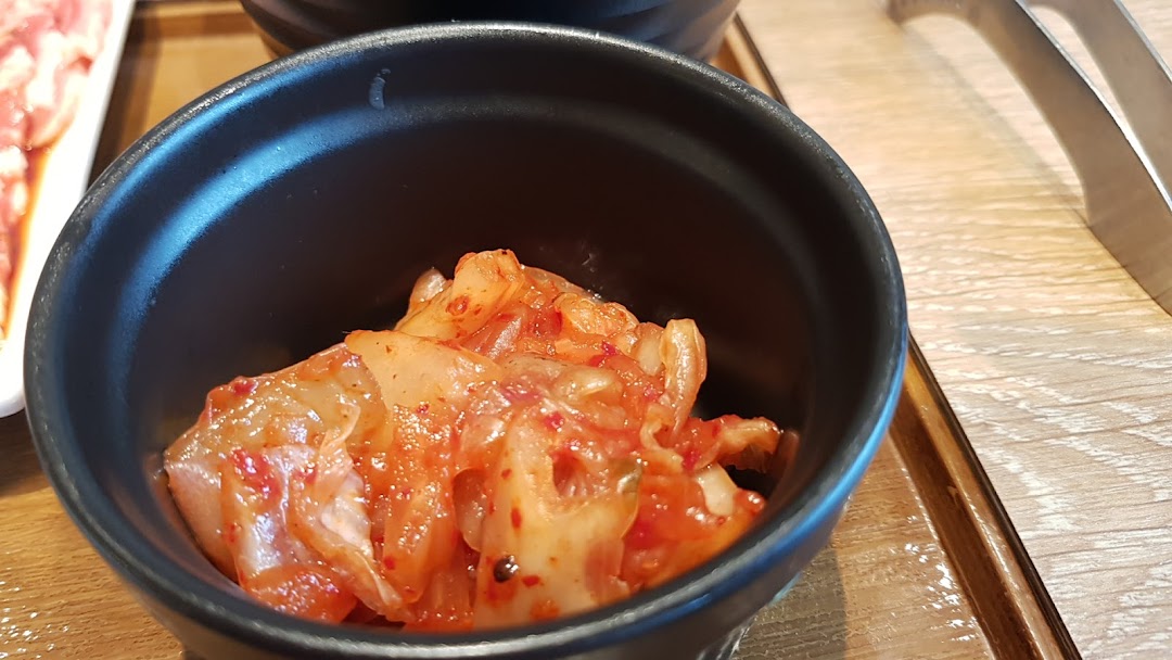 A close-up of a small black bowl of vibrant kimchi on a wooden table.