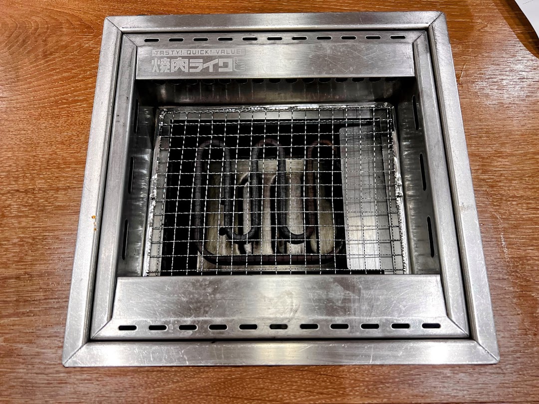 A close-up view of a clean, built-in yakiniku grill with a metal grate on a wooden table.