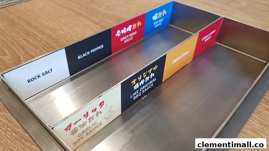 A close-up of a stainless steel condiment tray offering various sauces and seasonings.