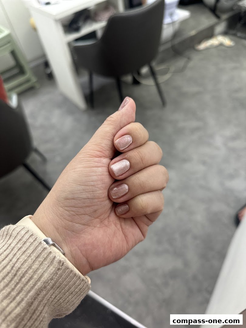 A close-up of a hand with perfectly manicured nails in a shimmering rose gold shade.