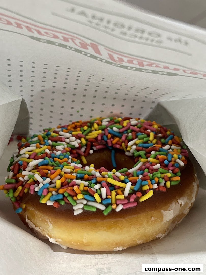 A close-up of a Krispy Kreme donut with chocolate frosting and colorful sprinkles.