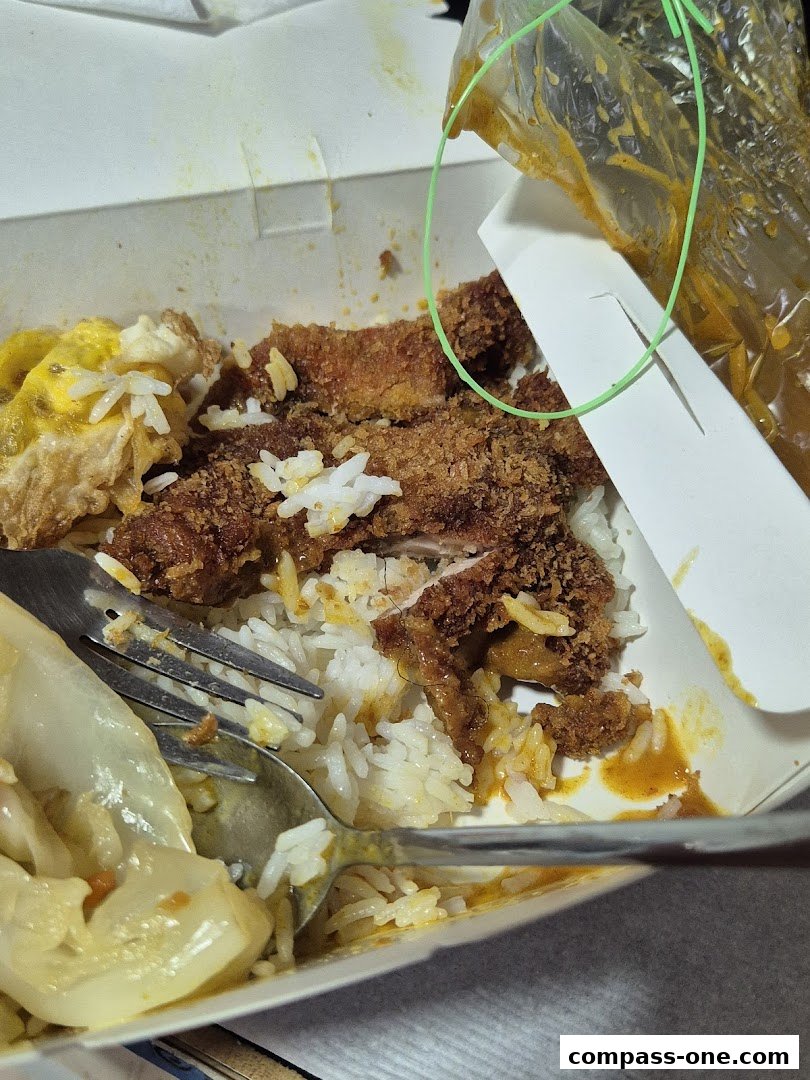 A close-up of a takeaway meal with rice, fried chicken, and a side dish.