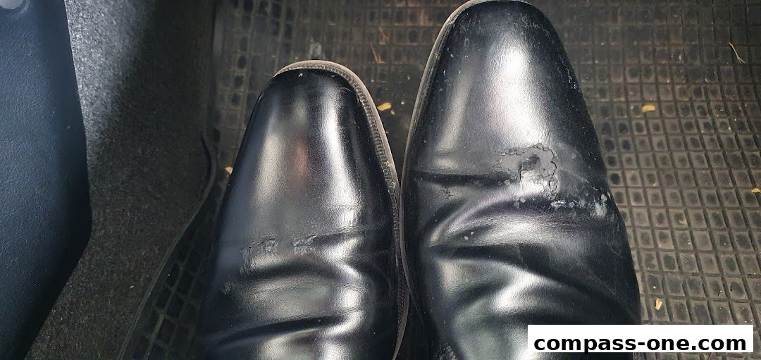 A close-up view of two black leather dress shoes with scuff marks and wear.