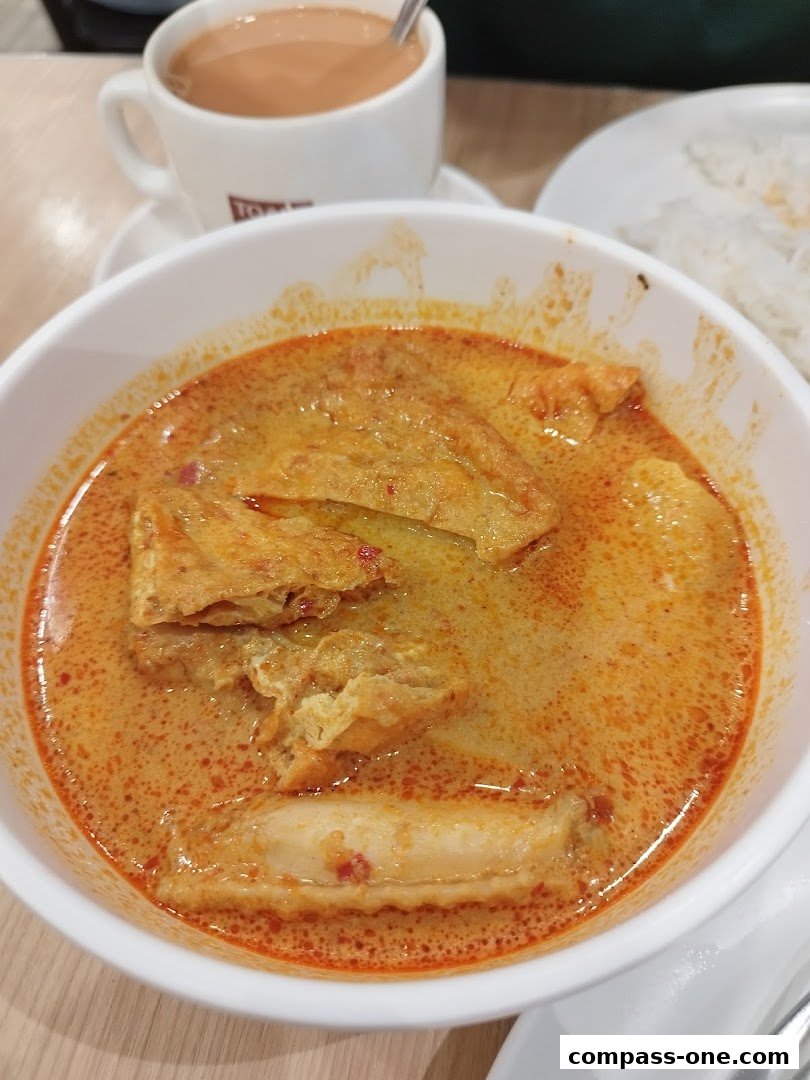 A bowl of curry with tau pok and fish cake, served with a cup of tea.