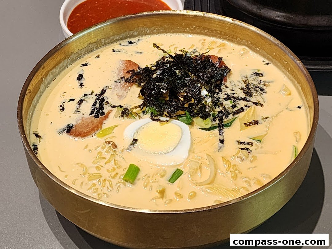 A close-up of a creamy Korean noodle soup dish with egg, seaweed, and chili sauce.