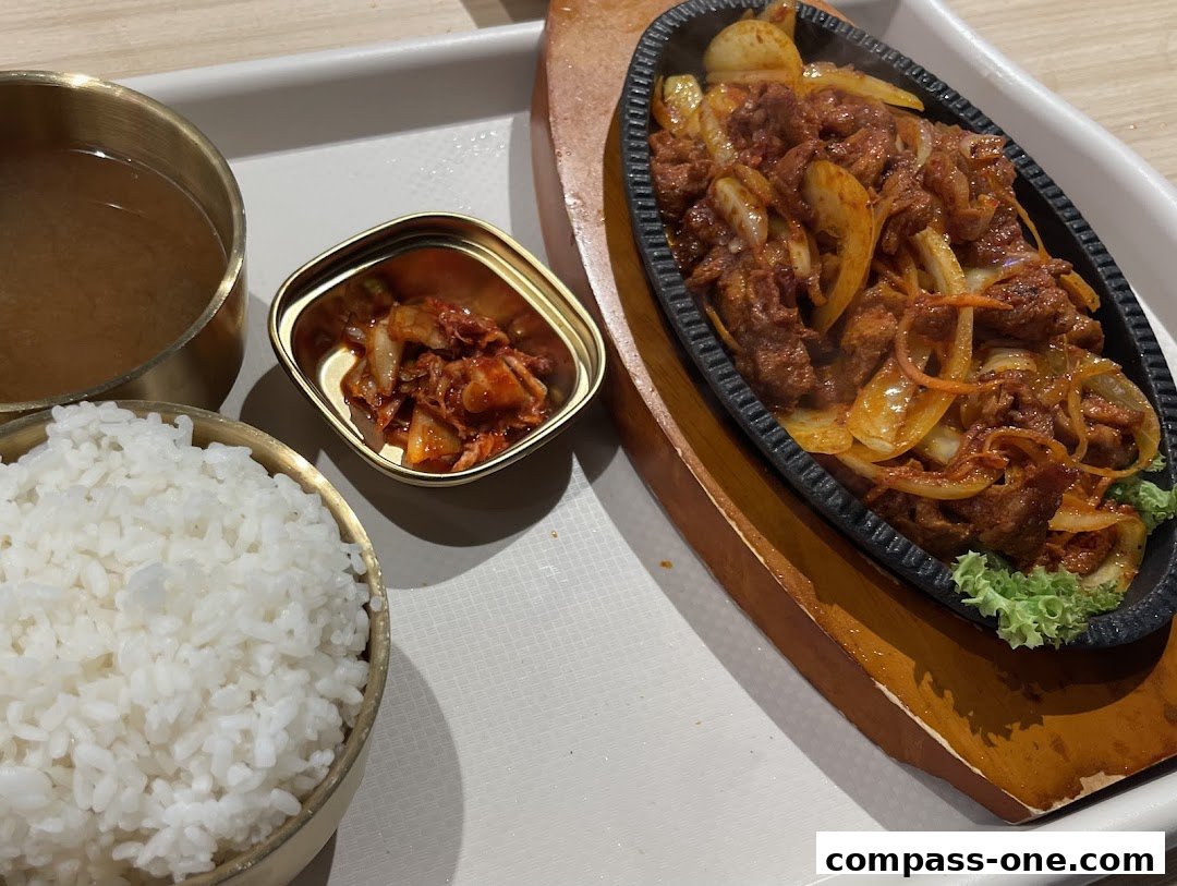 A sizzling Korean dish with meat, onions, and carrots, served with rice, kimchi, and soup.