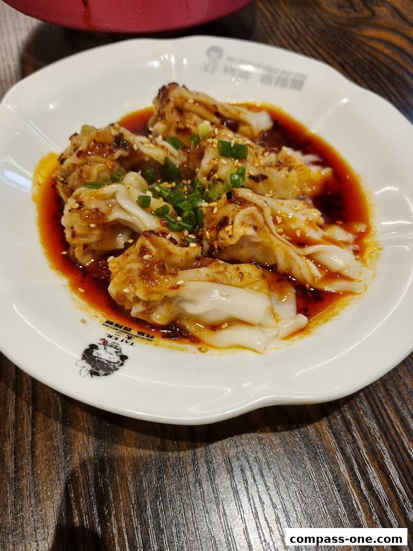A plate of wontons in chili oil, garnished with sesame seeds and scallions.