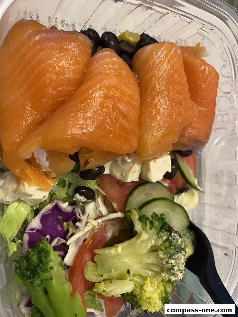 A close-up of a salmon salad with fresh vegetables and feta cheese in a clear container.