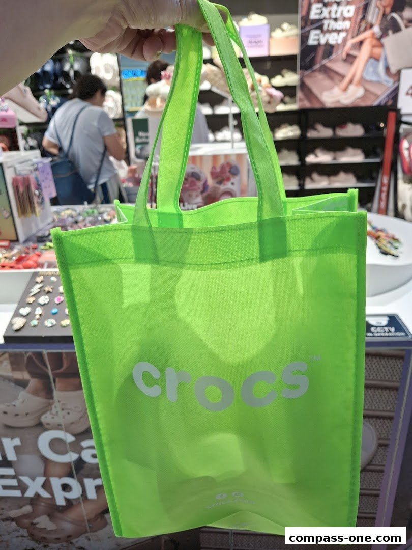 A bright green Crocs branded tote bag is held up in front of a store display.