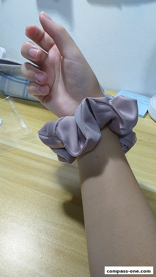 A person's wrist is adorned with a stylish, dusty rose scrunchie.