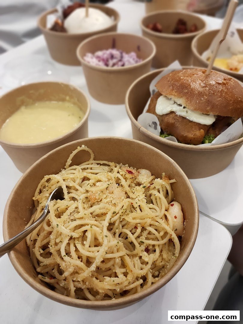 A close-up of a bowl of spaghetti with shrimp and a burger in the background.