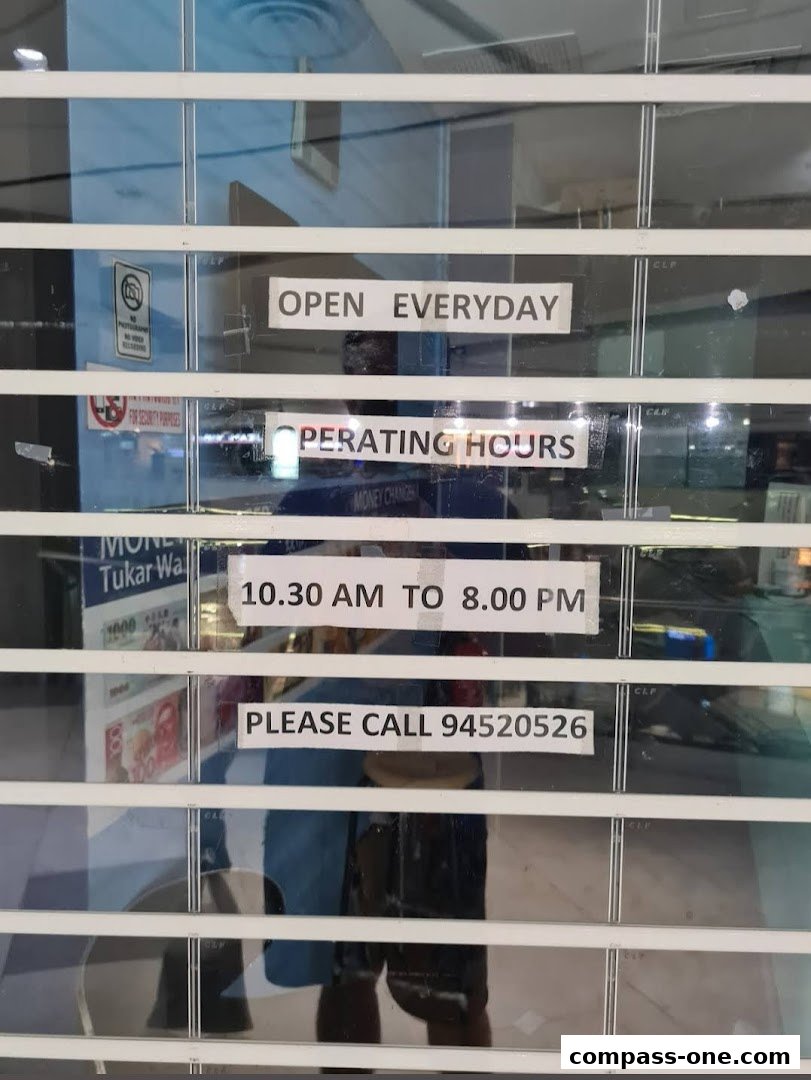 A shop front with a metal shutter displaying operating hours and contact information.