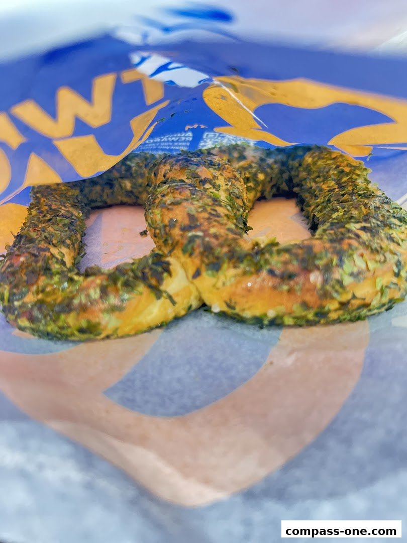 A close-up of a freshly baked pretzel with green seasoning inside an Auntie Anne's bag.