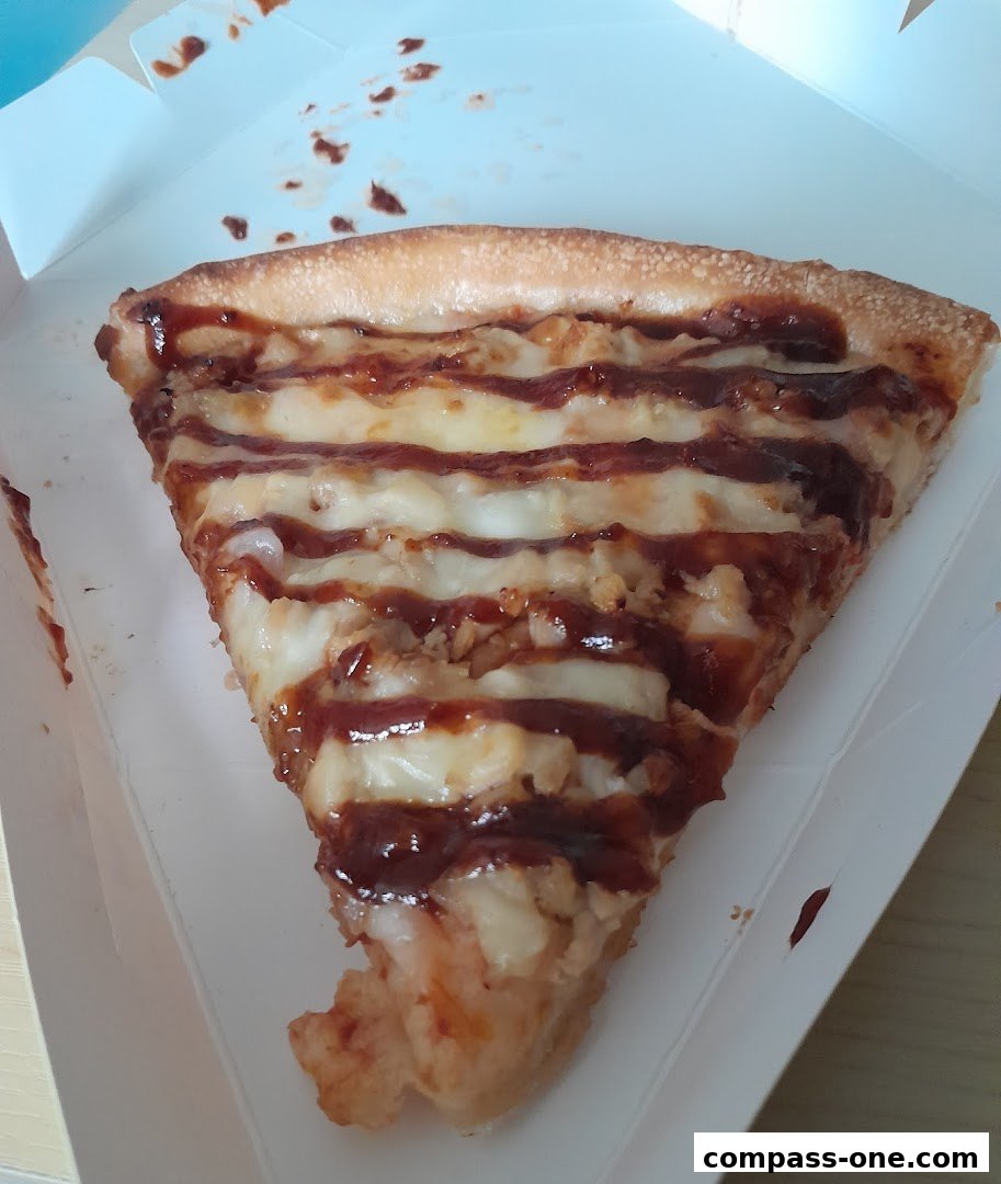 A slice of pizza with cheese and barbecue sauce in a white box.